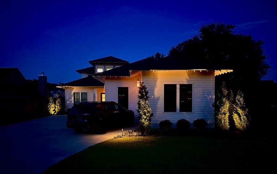 Home exterior at night with uplit cypress trees and path lighting