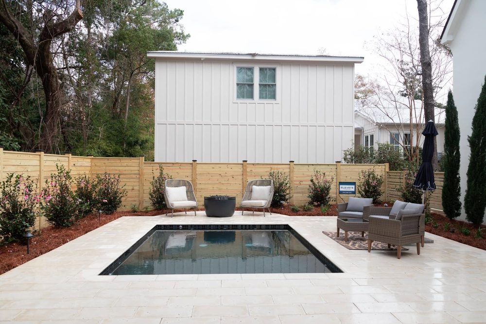 Rectangular pool with limestone deck, slat privacy fence and blooming camellias
